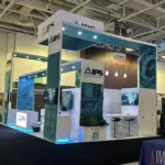 Open corner exhibition booth with teal canopy, LED-lit counter and screens, by a top exhibition services company in Anaheim