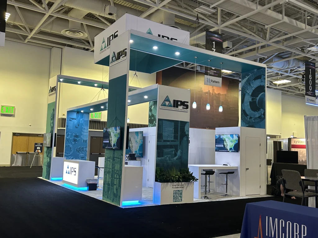 Open corner exhibition booth with teal canopy, LED-lit counter and screens, by a top exhibition services company in Anaheim
