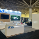 Small exhibition booth design with backlit logo, green wall display, TV screen and lit counters by exhibition stand companies in Dallas